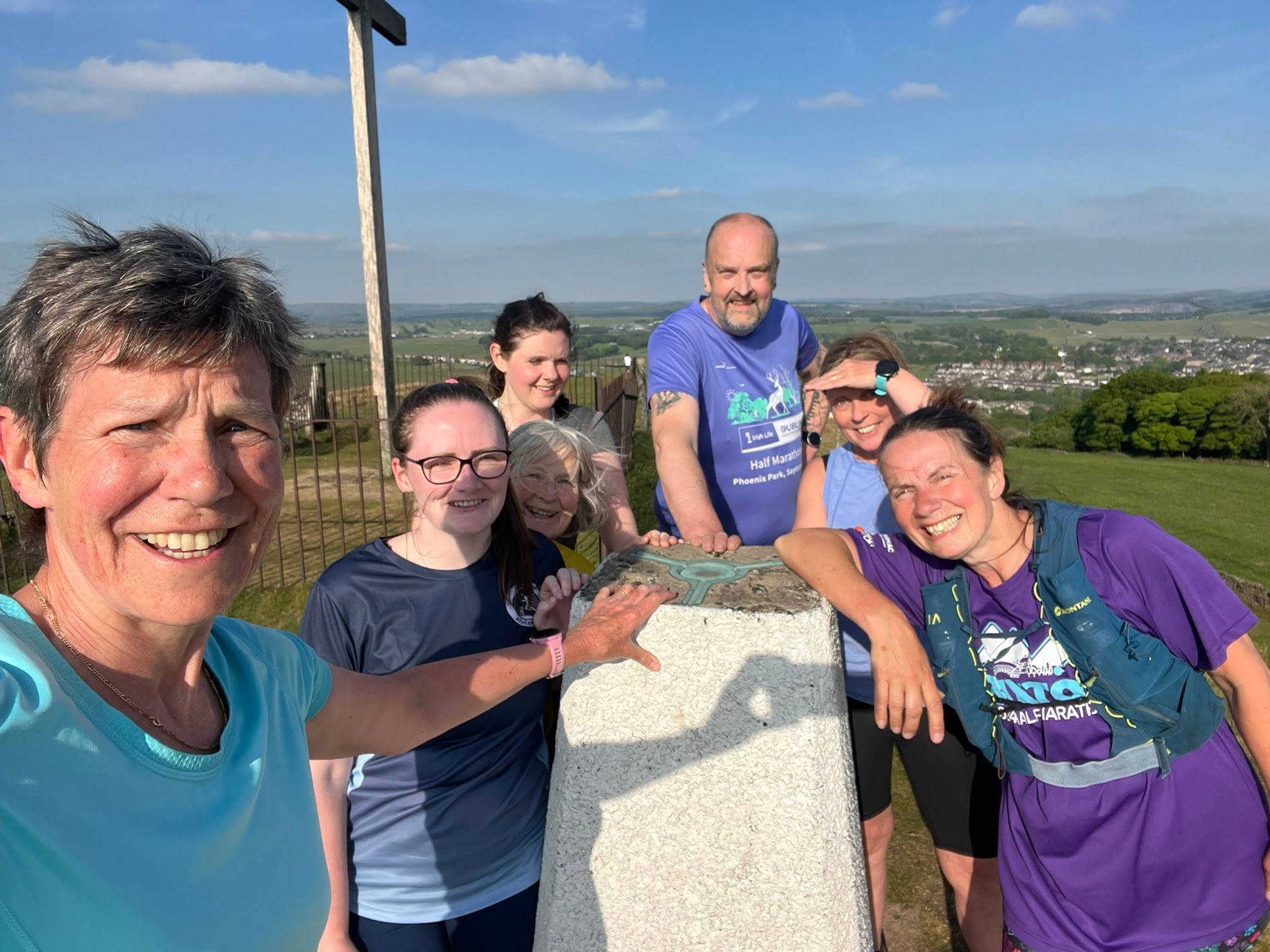 Club runners celebrating at a summit trig point